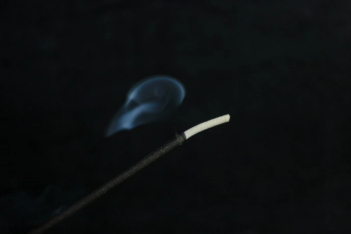 Incense stick burning with smoke against black background